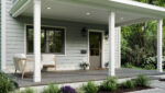 A modern house porch with white columns, gray siding, a wooden door, two chairs, potted plants, and landscaped greenery along a stone pathway. Trees and shrubs are visible in the background.