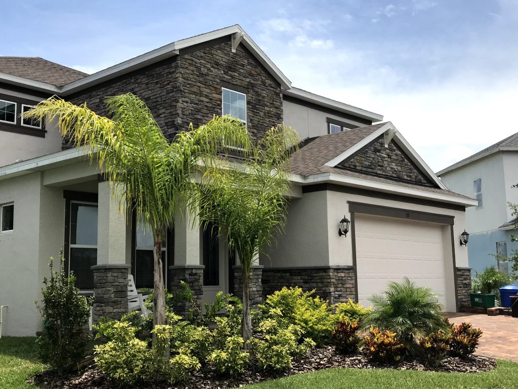 Western home design featuring a light stucco exterior paired with dark, modern ledge stone veneer and native landscaping.
