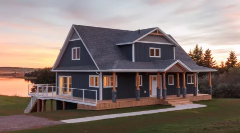 large water-front home at dusk with a wrap around front porch