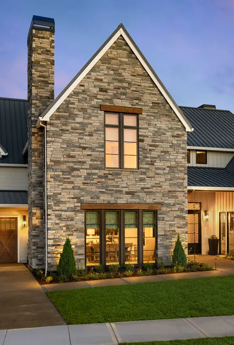 Modern home exterior with stone siding, dark trim, and evening lighting.